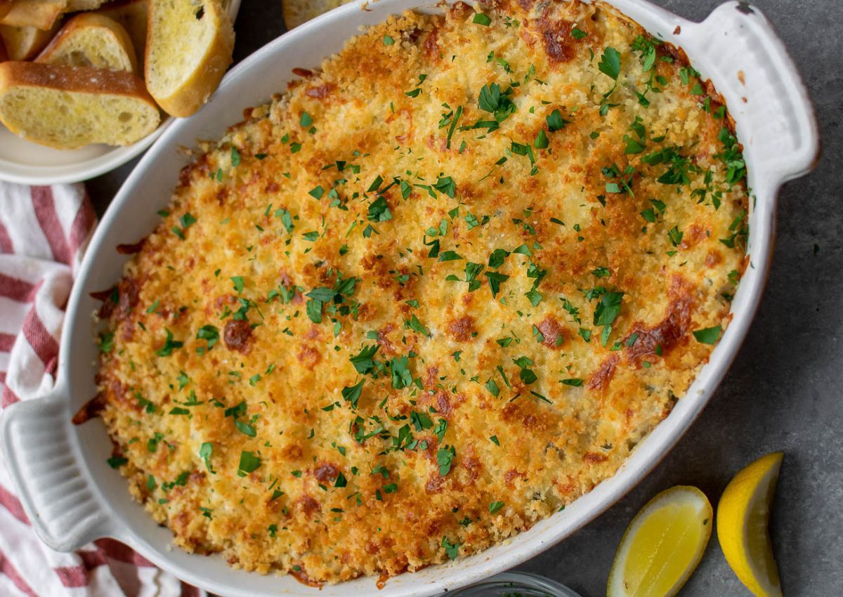 A baked dish in an oval casserole, topped with a golden breadcrumb crust and garnished with chopped parsley.