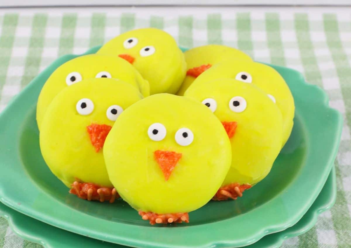 Oreos decorated like chicks on a green plate.