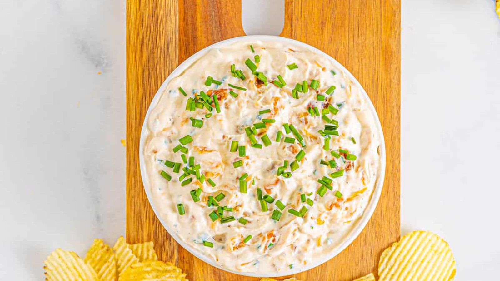 Bowl of greek yogurt onion dip on a cutting board with Ruffles.