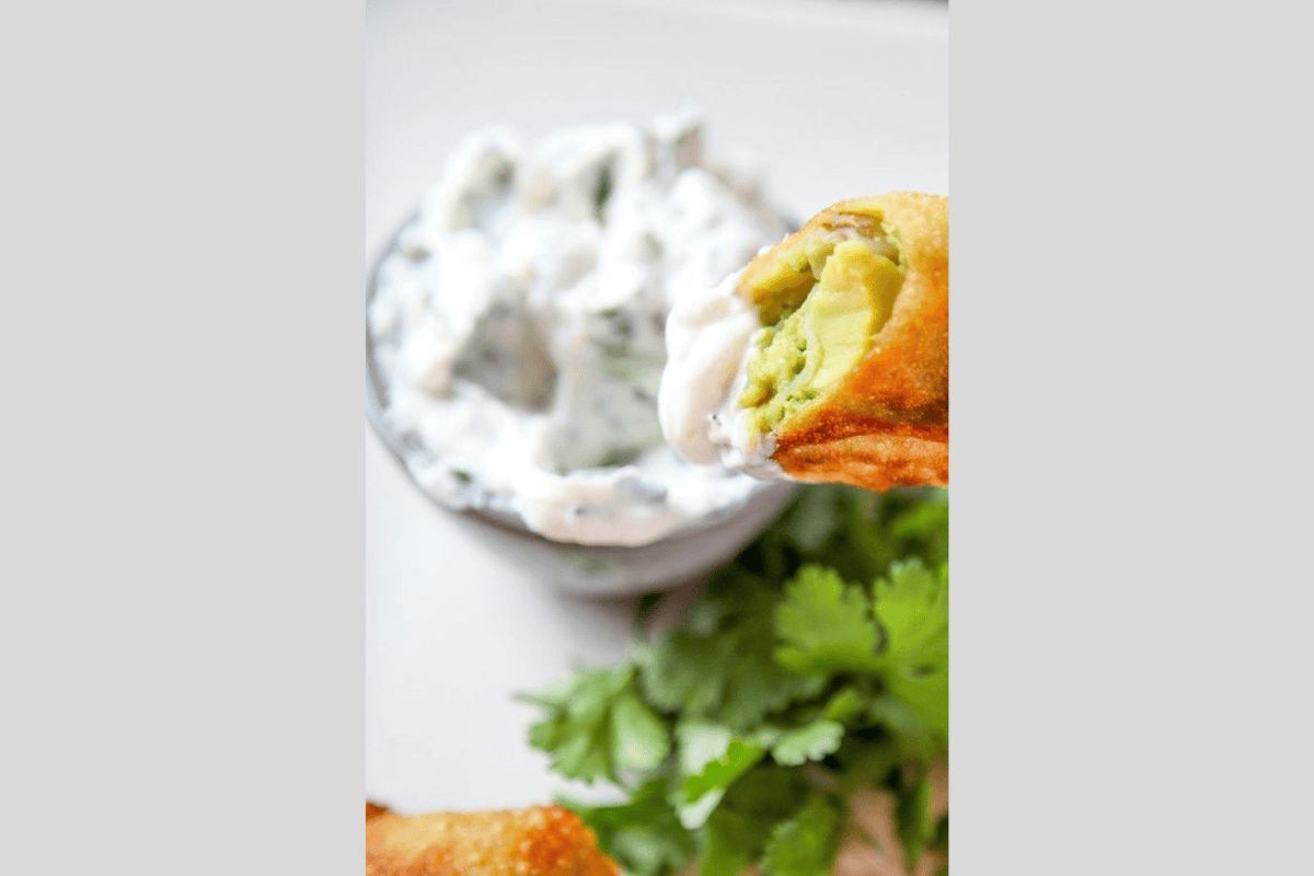 An avocado egg roll being dipped into a creamy cilantro sauce.