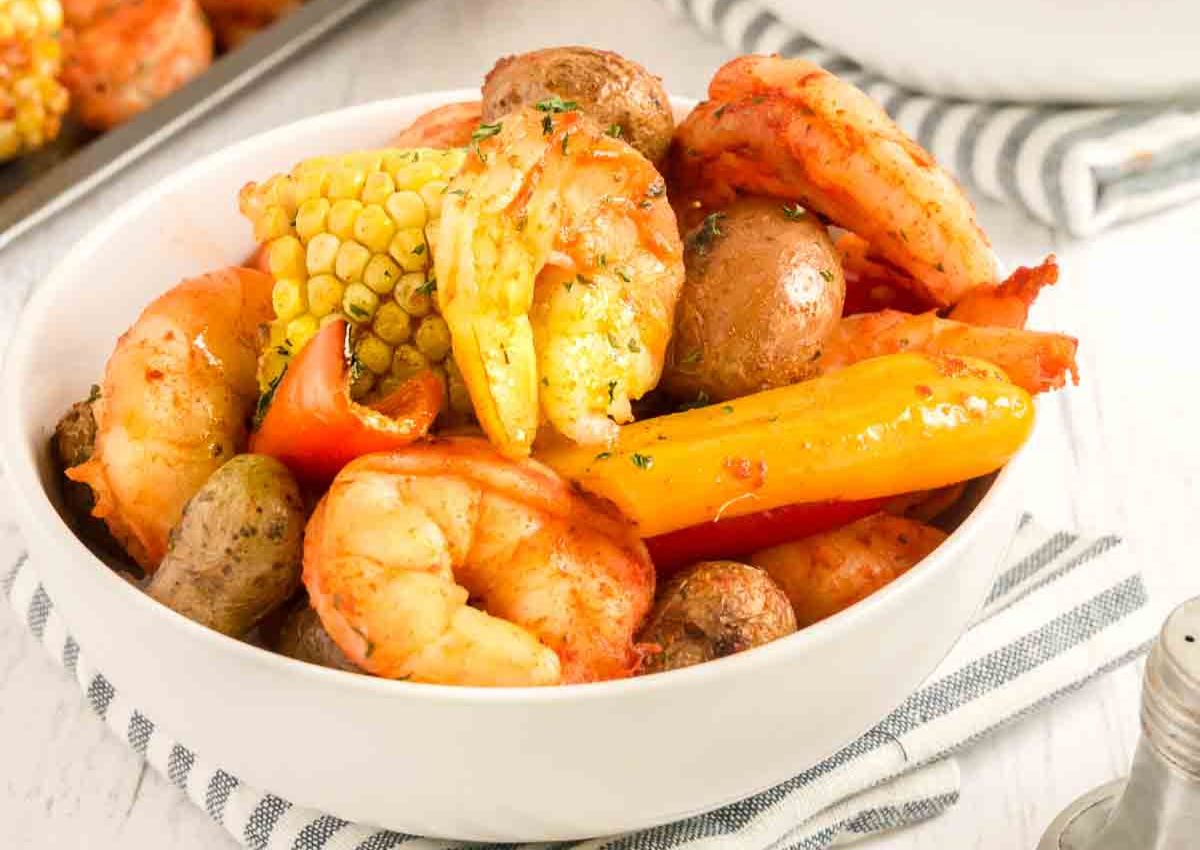 A bowl filled with cooked shrimp, halved corn on the cob, small round potatoes, and sliced bell peppers.