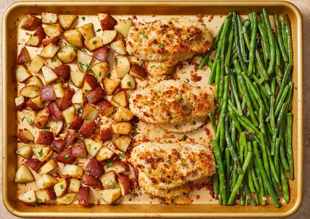 A baking sheet with roasted red potato chunks on the left, three breaded chicken breasts in the middle, and cooked green beans on the right.