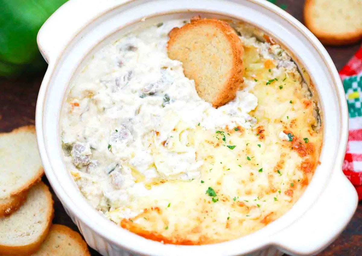 A white ceramic dish filled with hot, baked creamy cheese dip, slightly browned on one side.