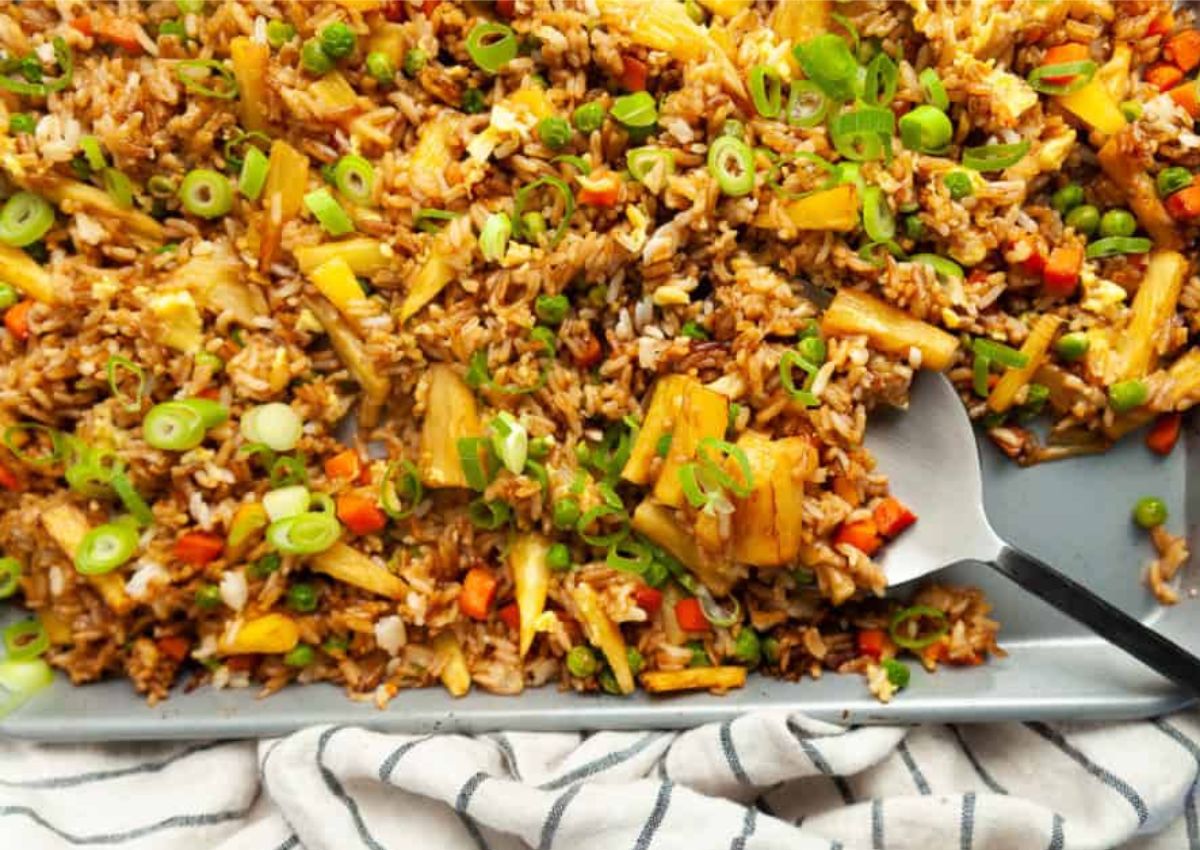 A close-up of pineapple fried rice on a rectangular plate, garnished with chopped green onions.