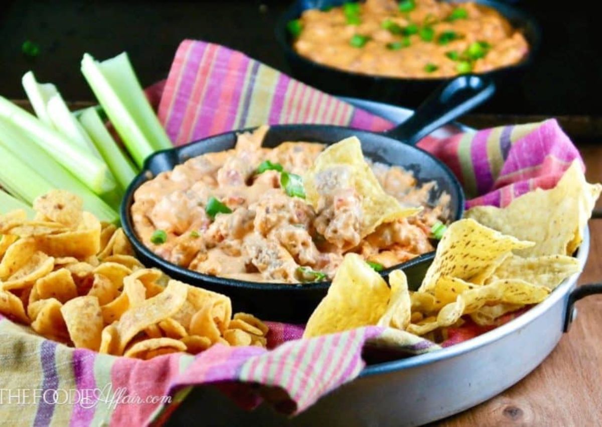 A black skillet filled with creamy dip sits on a plate surrounded by tortilla chips and Fritos.