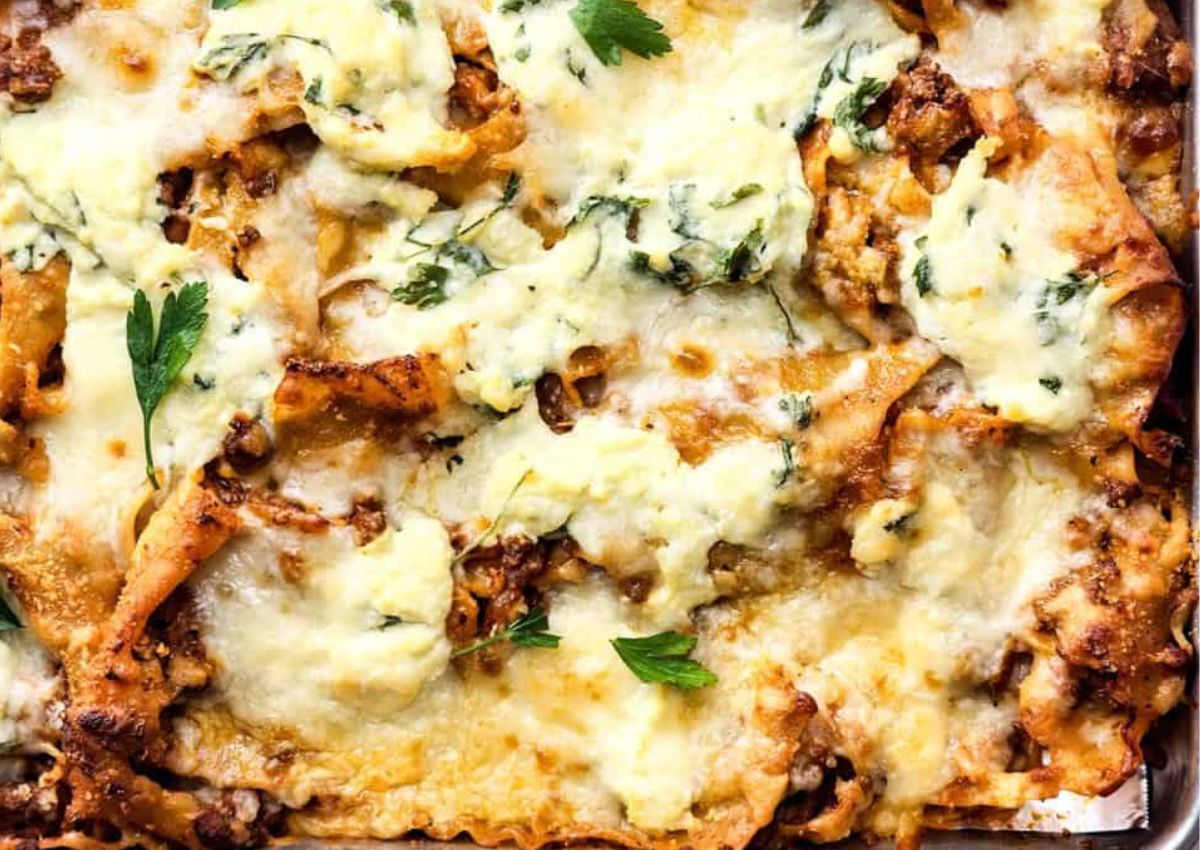 Close-up of a baked lasagna with visible layers of pasta, meat, and melted cheese. Fresh parsley leaves are scattered on top, adding a touch of green.