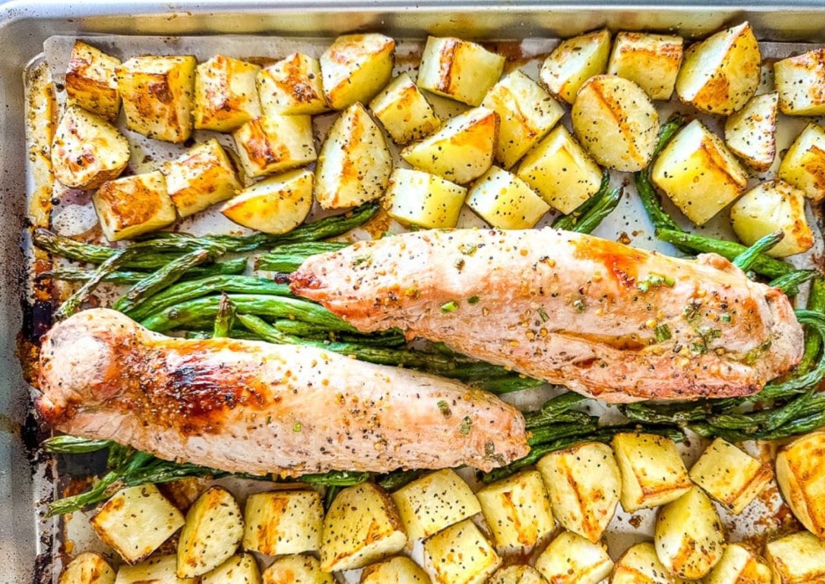A baking sheet with roasted potatoes, green beans, and two seasoned pork tenderloins.