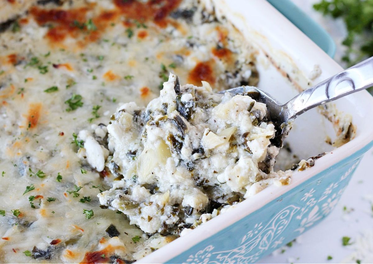  A baking dish filled with creamy spinach artichoke dip, partially scooped out.