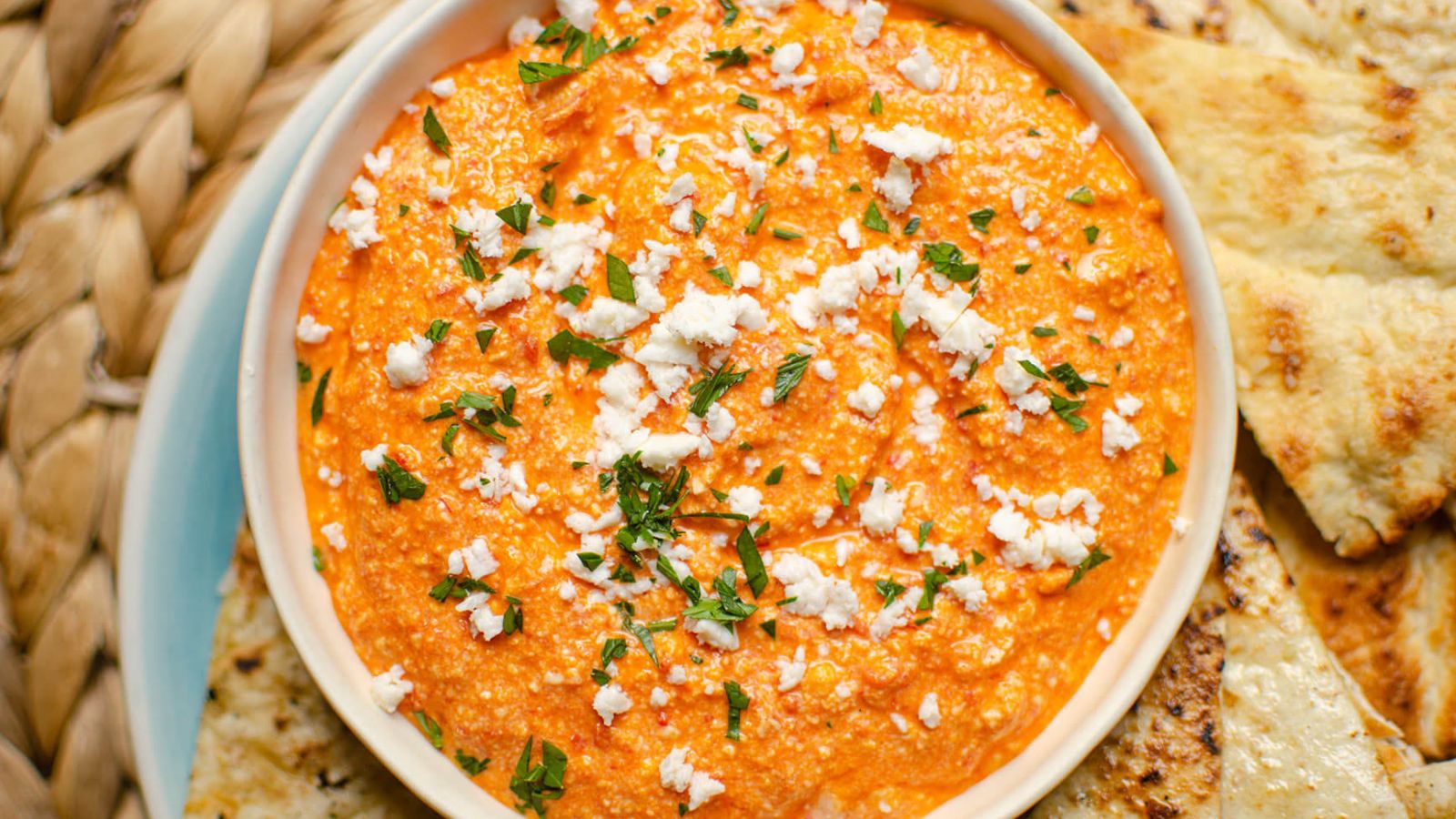 Bowl of tirokafteri dip topped with feta cheese.