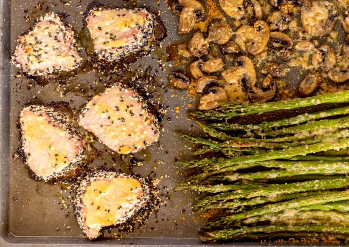 A baking sheet with four crusted tuna pieces on the left, sautéed mushrooms at the top, and roasted asparagus spears on the right. 