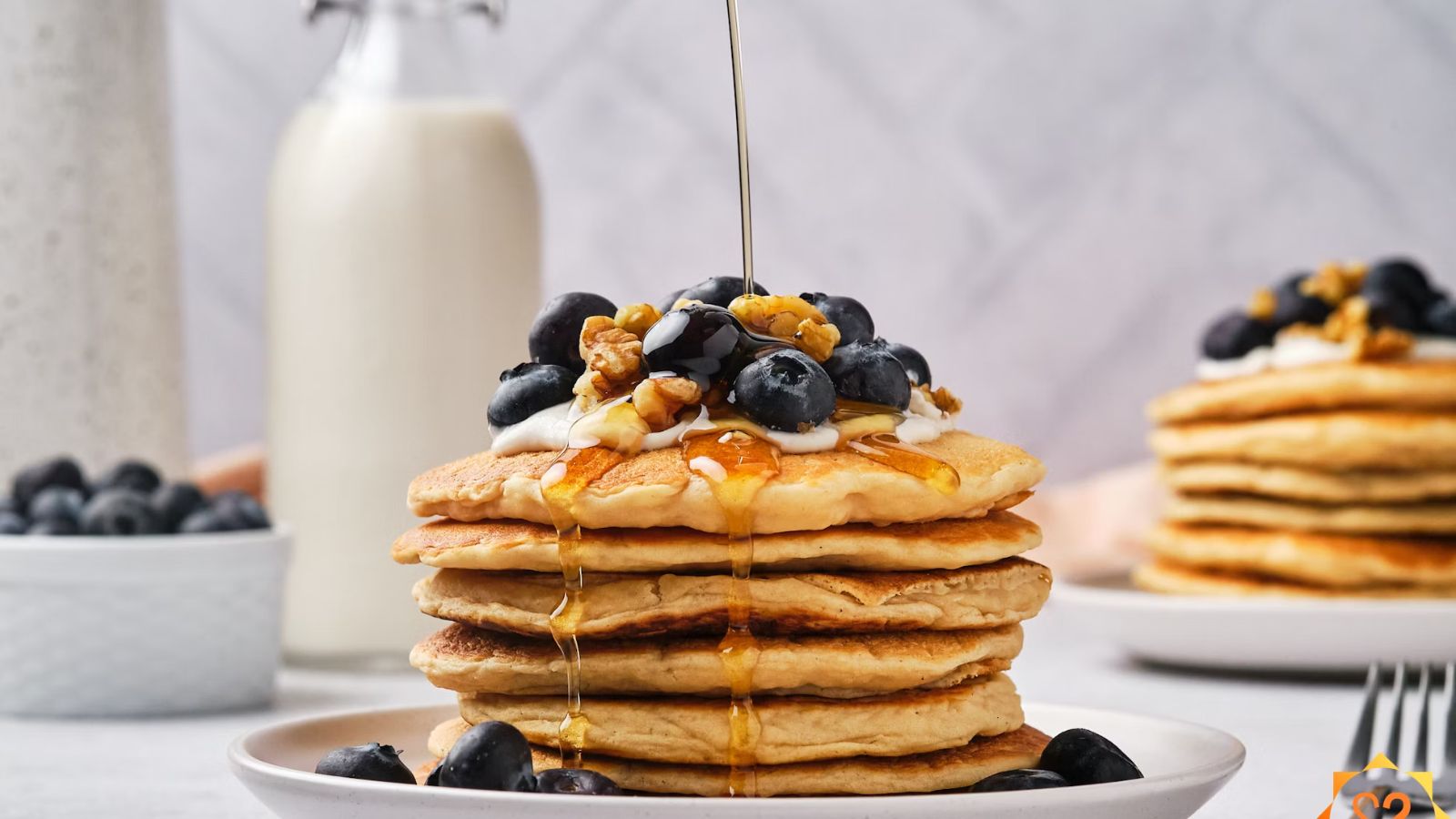 Vegan protein pancakes on a plate topped with blueberies and syrup being poured on top. 