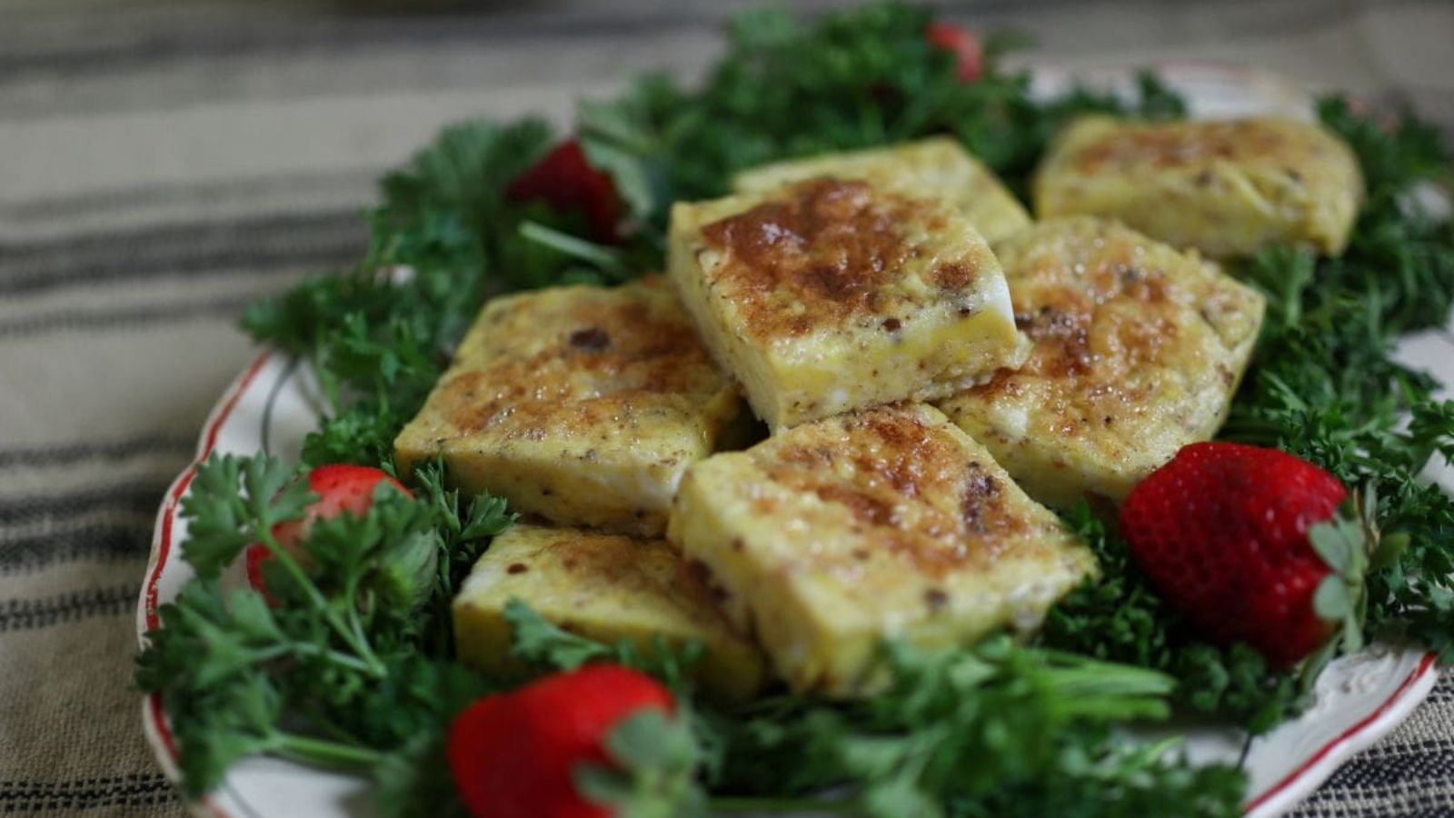 Old fashioned omelete cut into squares on a plate with parsley and strawberries. 