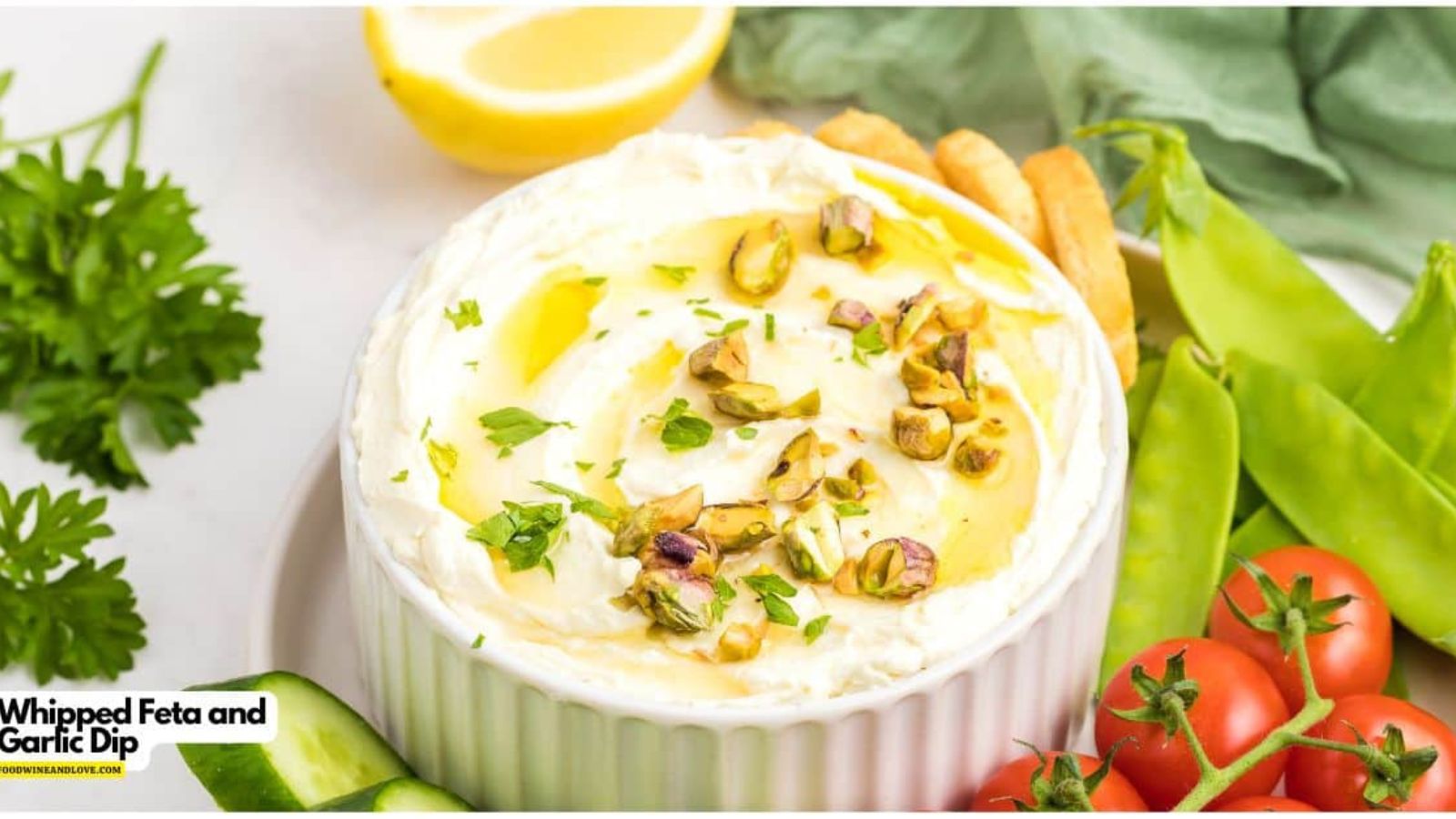 Small bowl fill of whipped feta and garlic dip topped with olive oil and pistachios.