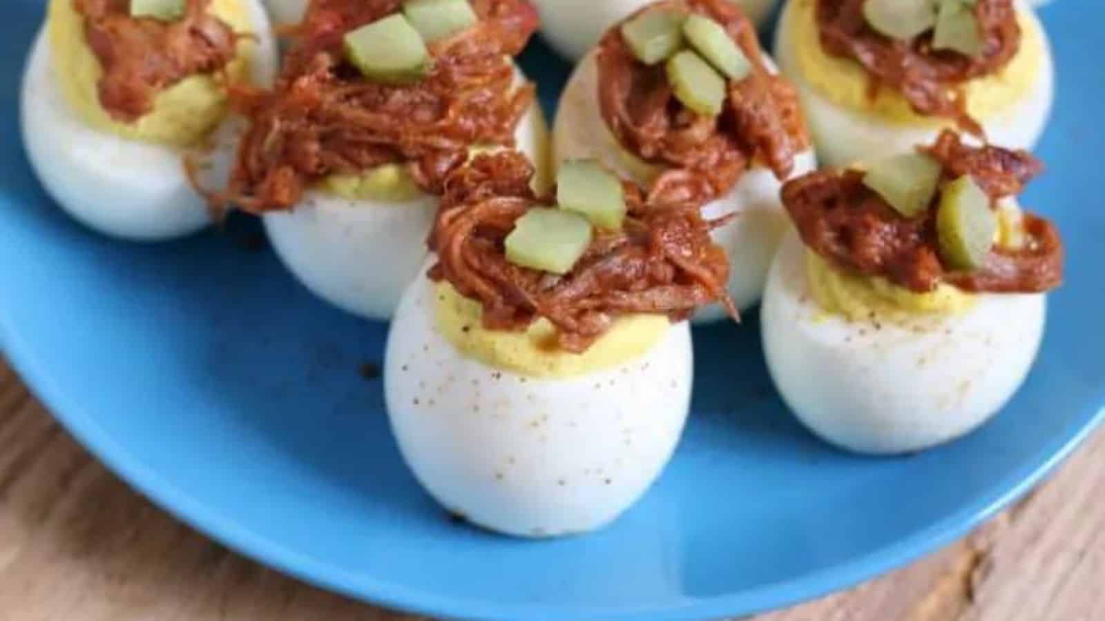 Deviled eggs topped with pulled pork on a blue plate.