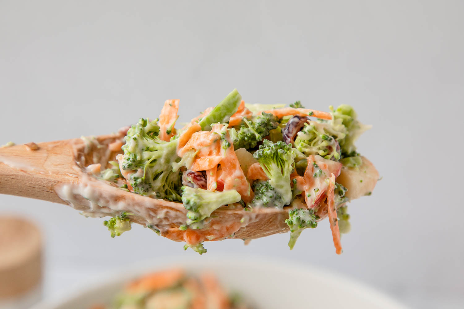 Wooden spoonful of broccoli apple salad held in the air.