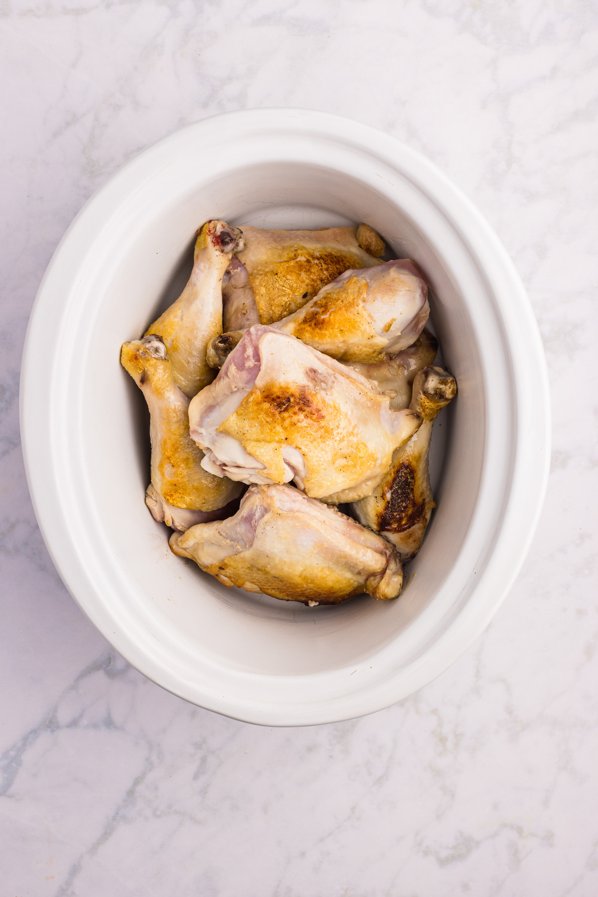 Browned chicken pieces in a white slow cooker.