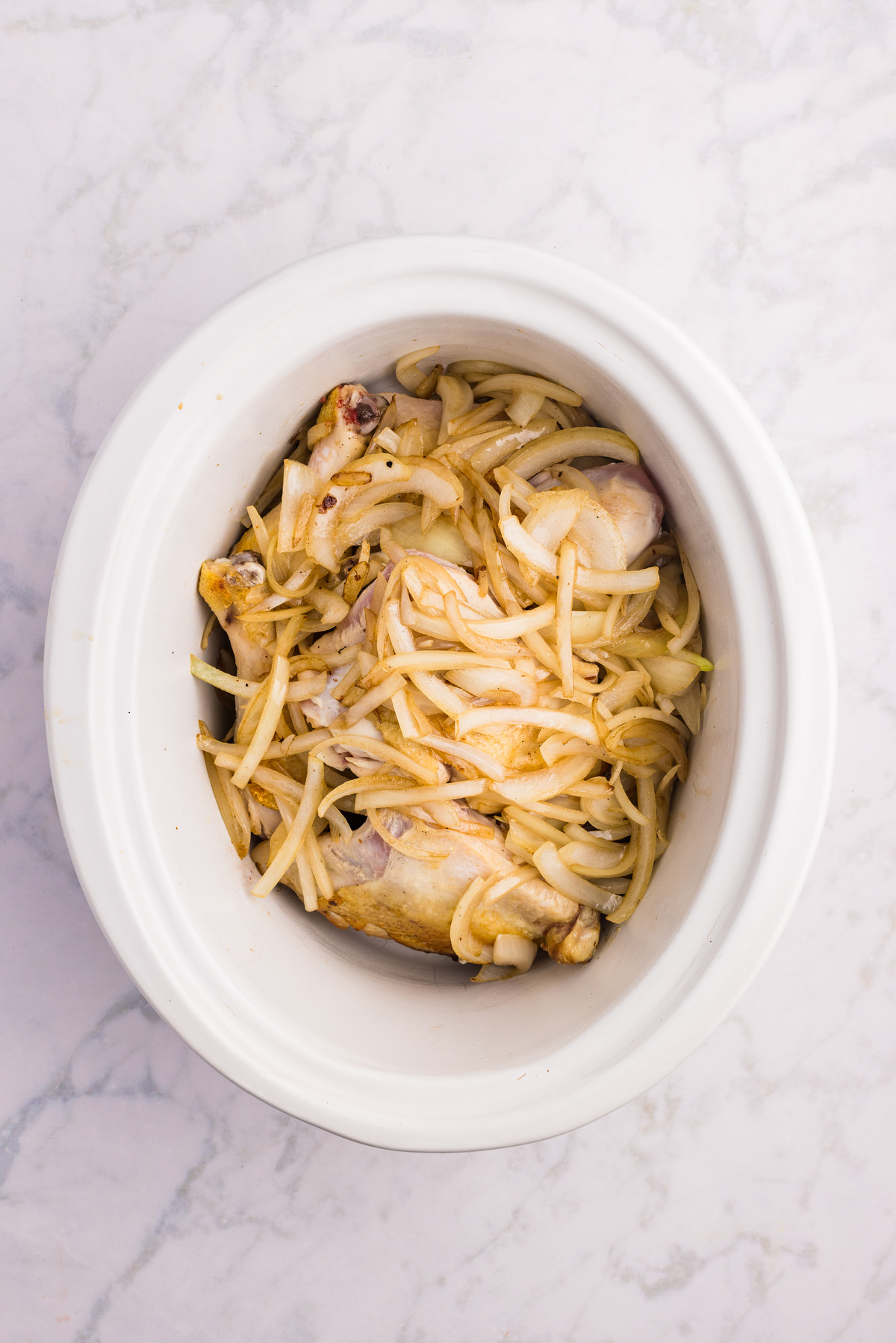 Chicken topped with sliced onion in a slow cooker.
