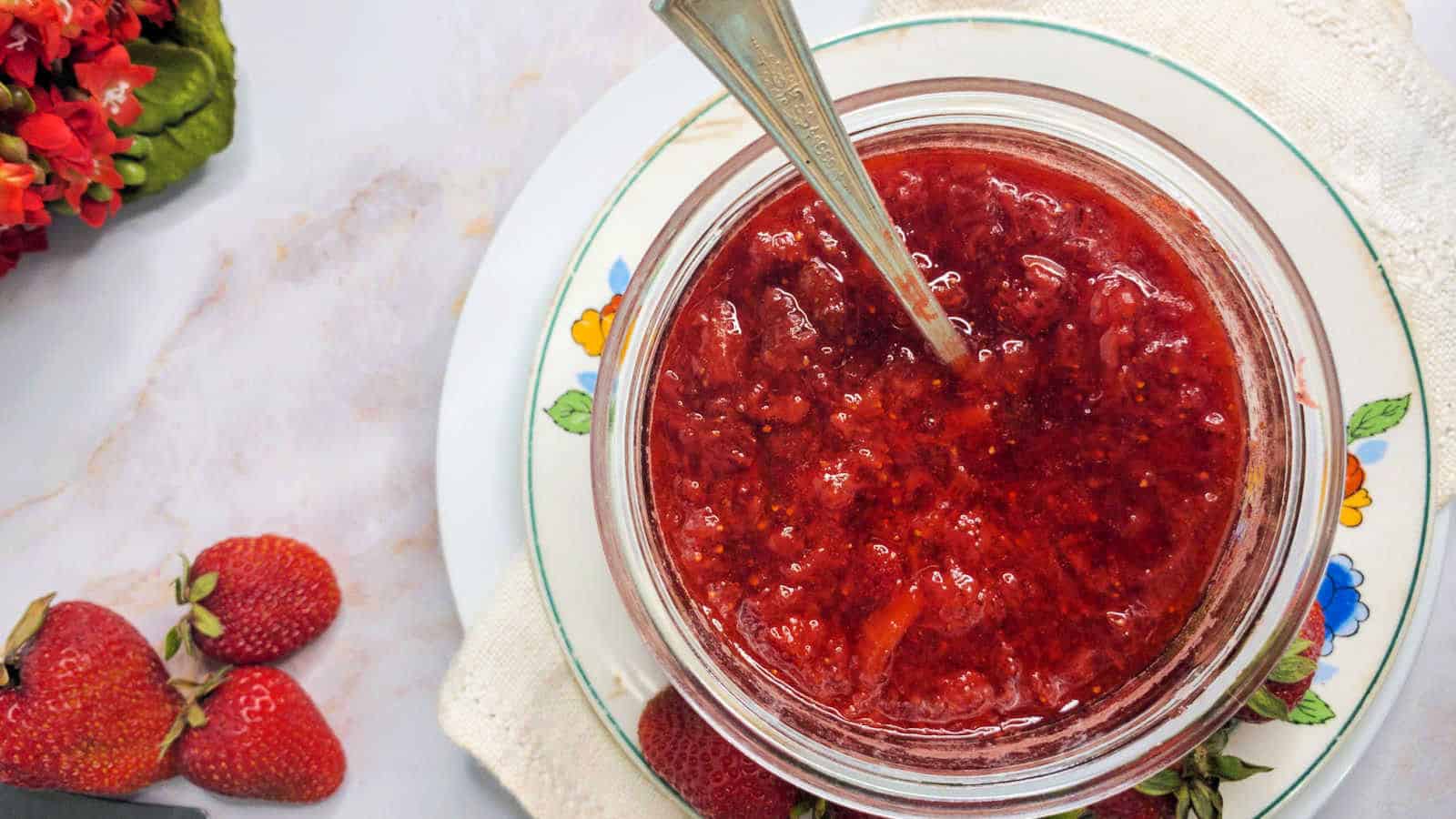 Jar full of strawberry jam on a small plate.