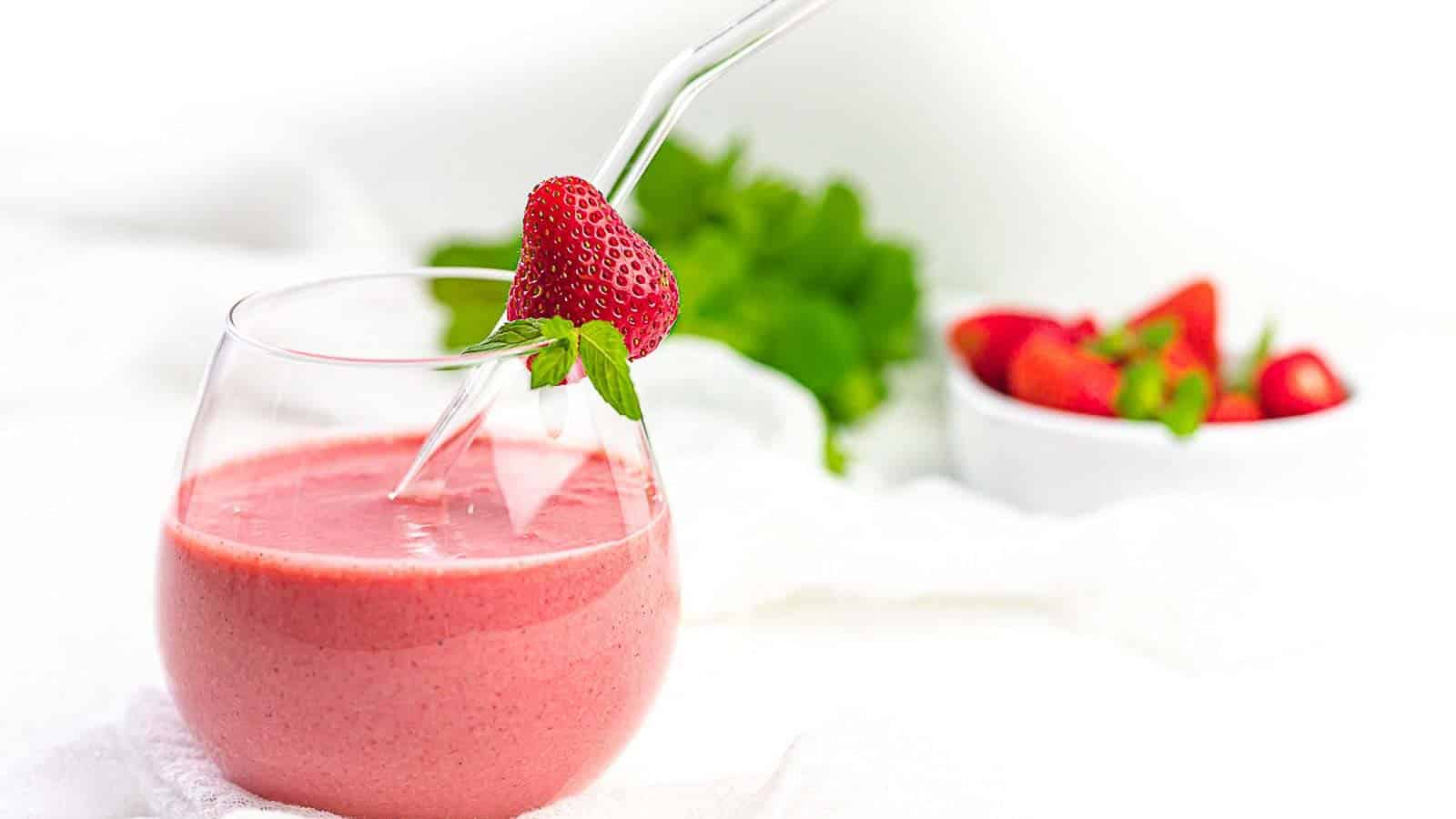 Glass full of strawberry smoothie with a strawberry on the rim.