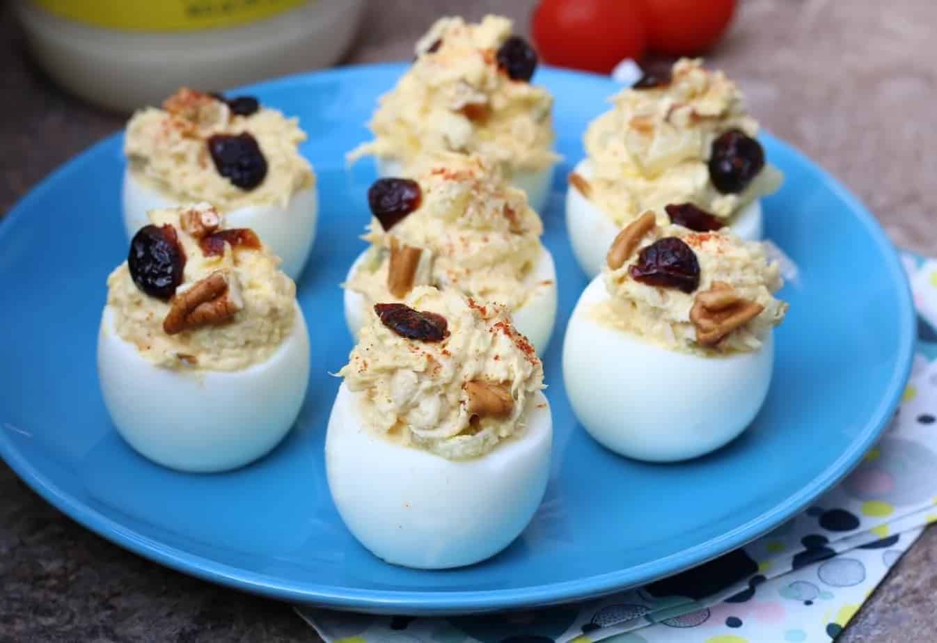 Deviled eggs topped with pecans and dried cranberries on a blue plate.