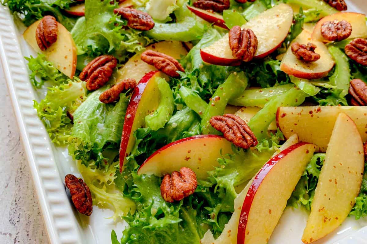 Apple and pecans on a bed of lettuce on a platter.