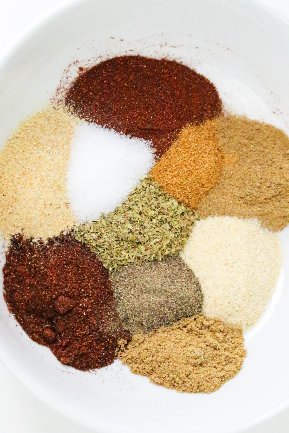 Ten different spices in a mixing bowl before whisking them to blend.