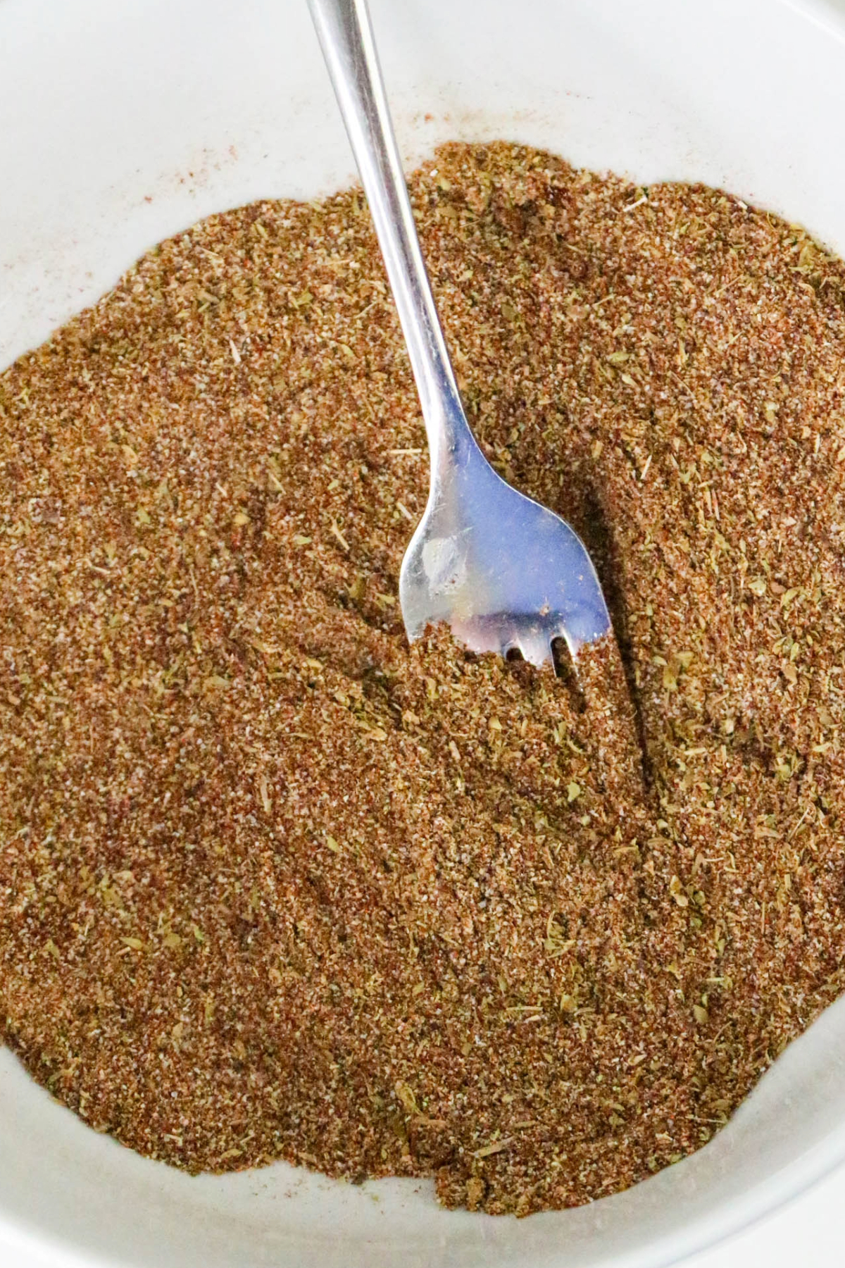 spices in a white bowl whisked with a silver fork.