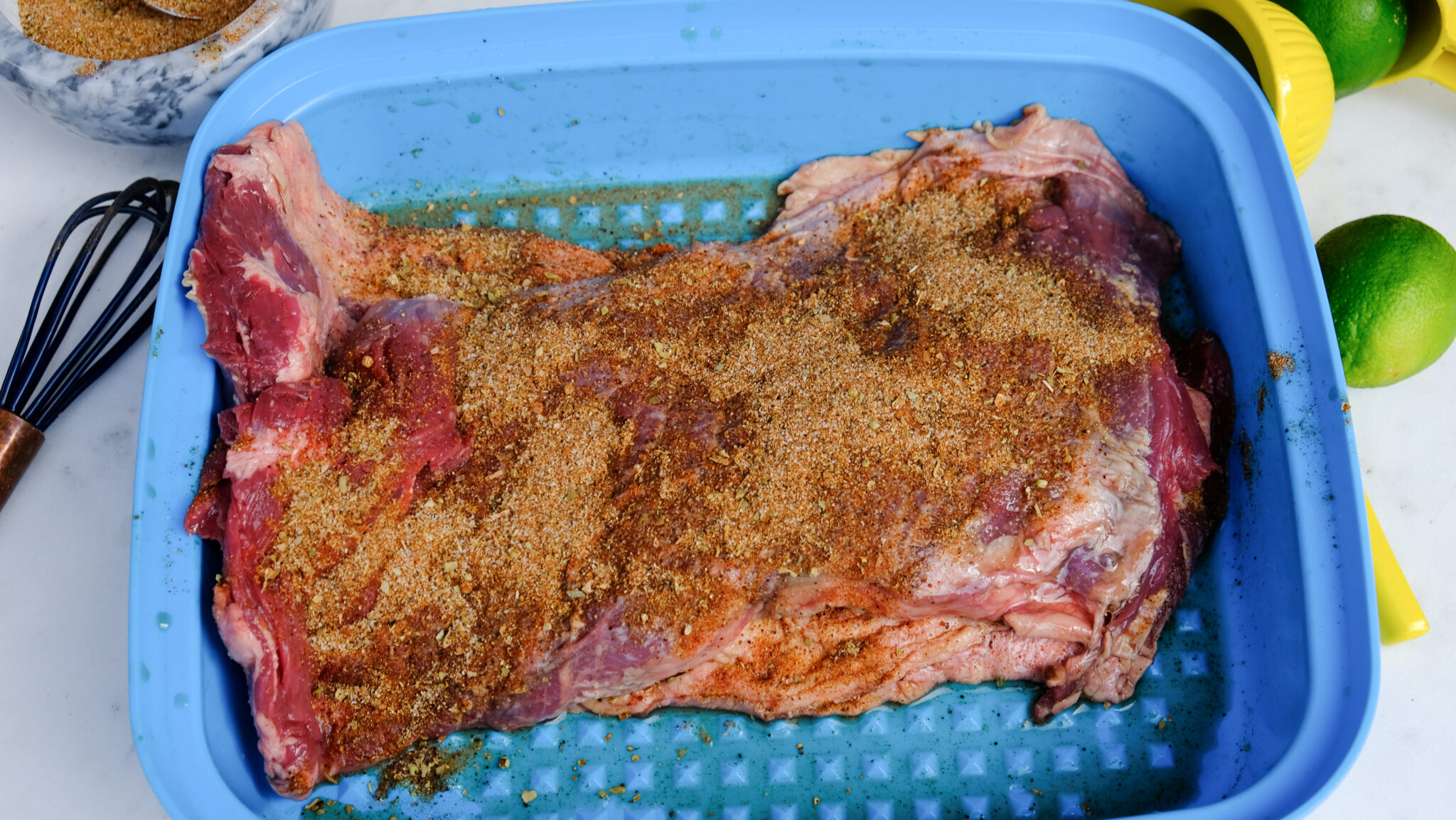 Skirt steak with carne asada seasoning and lime juice in a meat marinading plastic container.