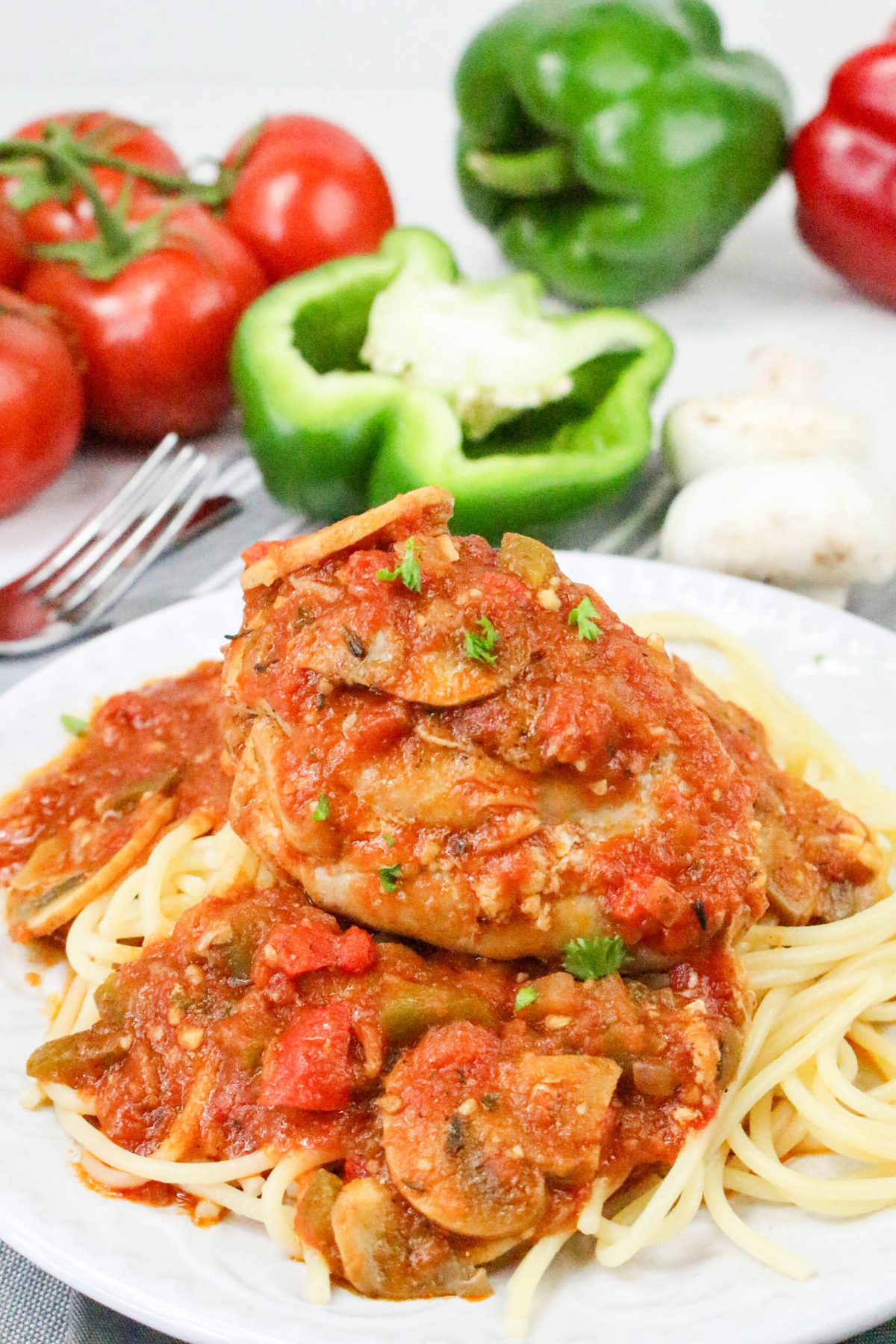 Chicken cacciatore over pasta on a white dinner plate.