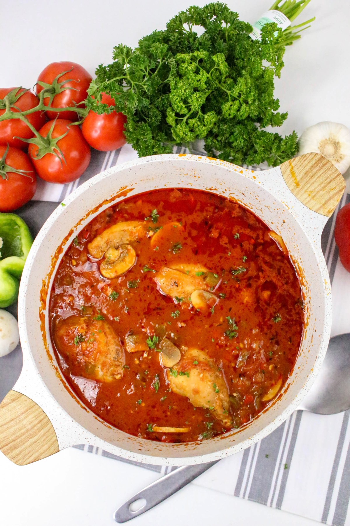 Top view of chicken cacciatore in wine tomato broth in a white Dutch oven before serving.
