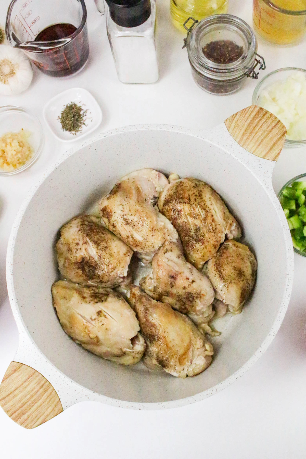 Sautéed chicken thighs seasoned with salt and pepper in a white pot.