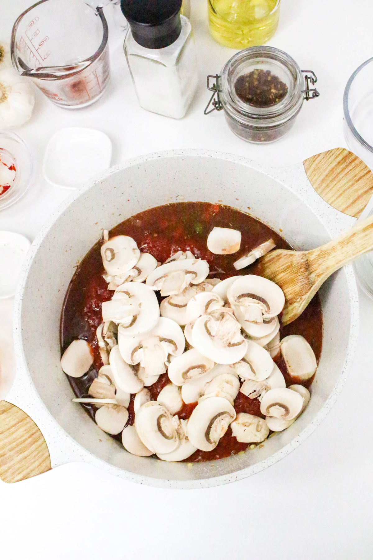 Fresh mushrooms added to a cooking pot with tomato based sauce.