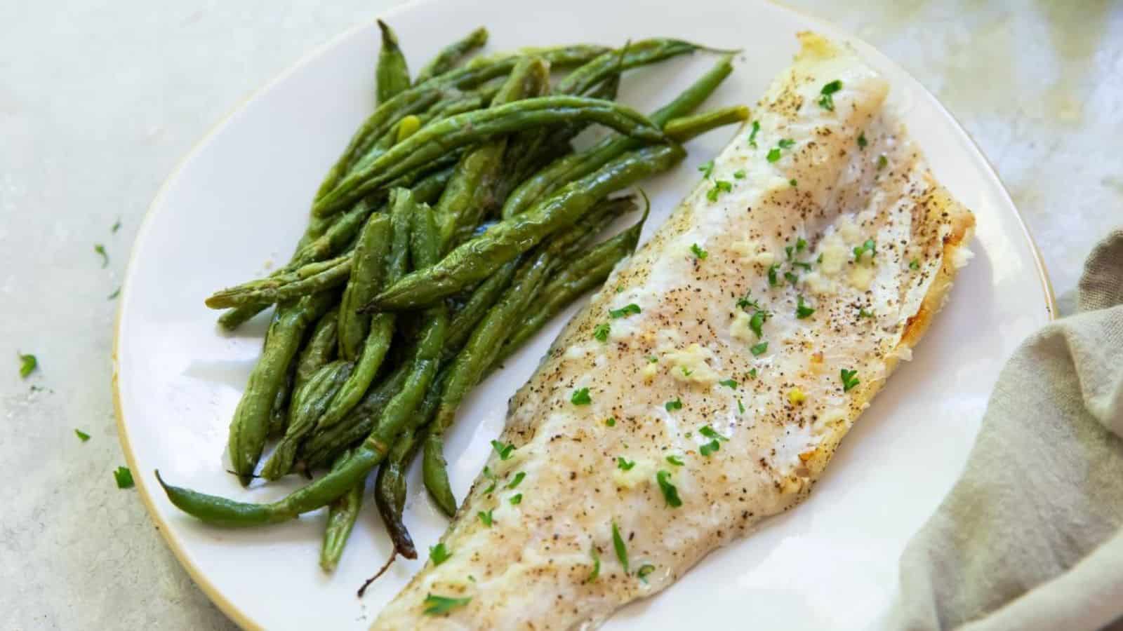 Broiled white fish on a plate with green beans.