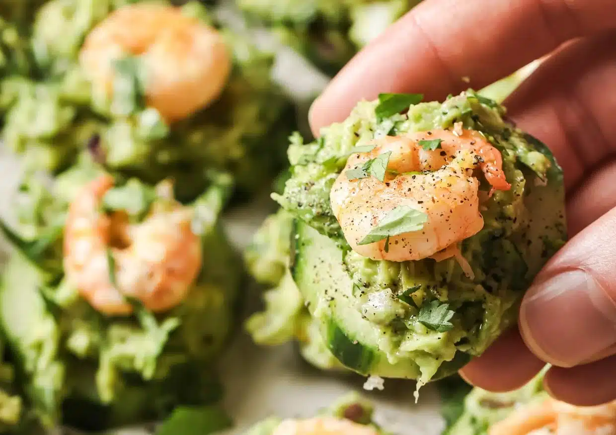 Cucumber shrimp appetizer held in a person's hand.