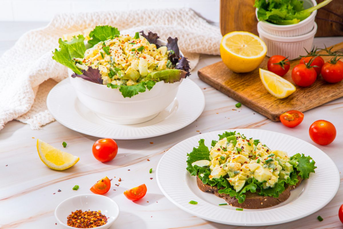 Egg salad on white serving plates and bowl with tomatoes on the side.