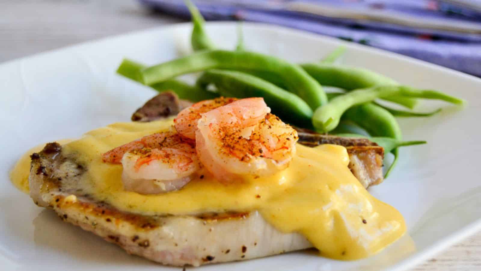 Pork chop on a plate topped with shrimp.