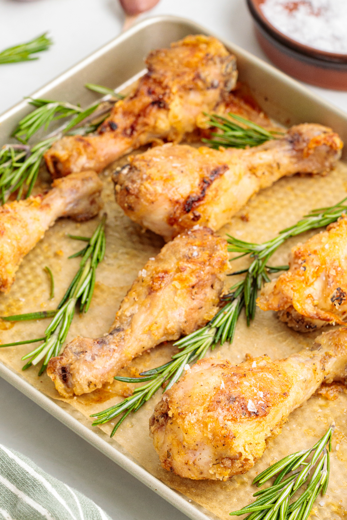 Baked drumsticks out of the oven with rosemary sprigs on the side.