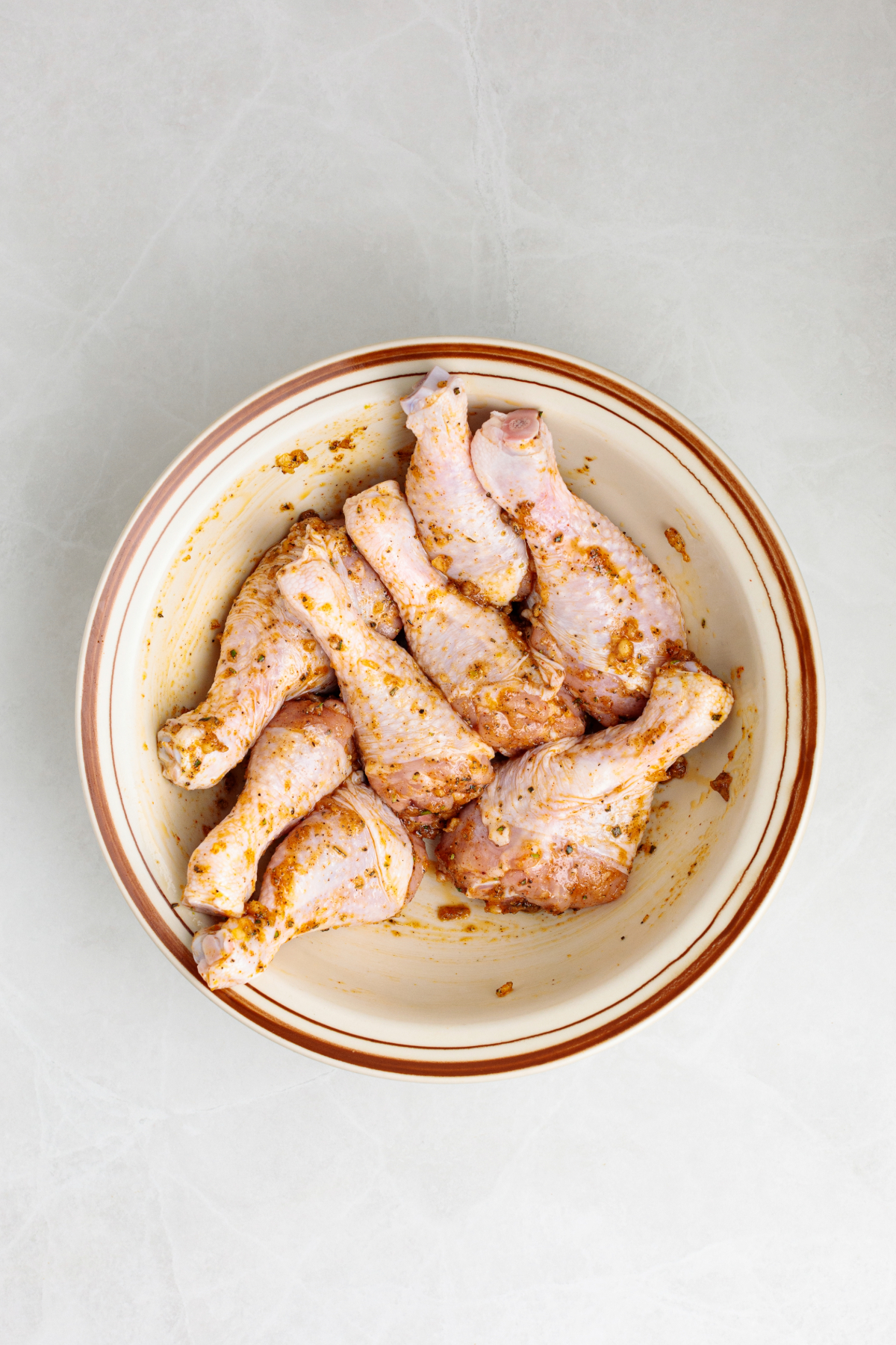 Chicken in a mixing bowl coated with spices.