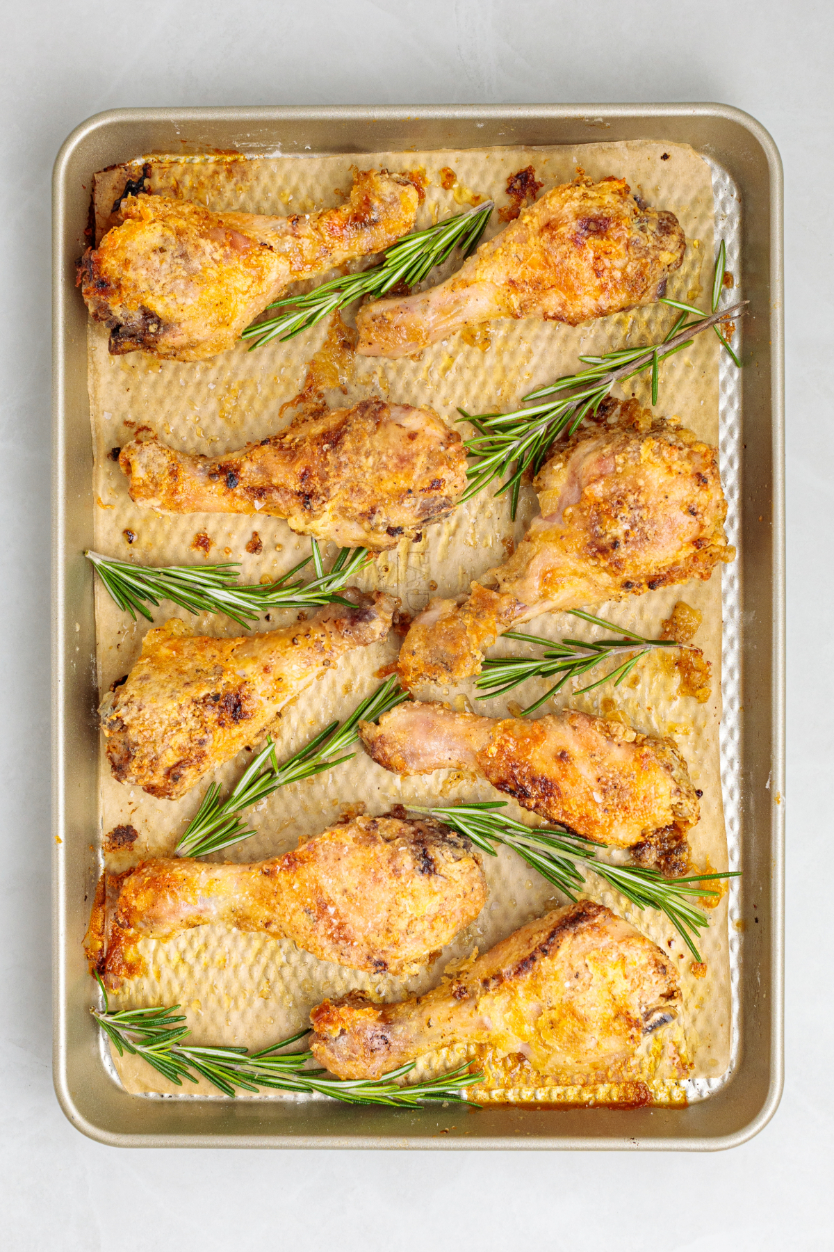 Baked drumsticks on a silver baking sheet with rosemary sprigs.