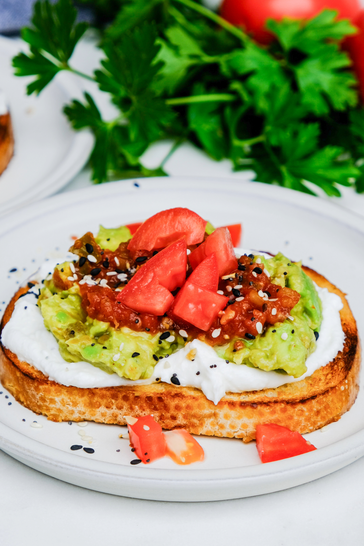 Toast with cottage cheese and avocado topped with salsa and diced tomato on a white dish. 