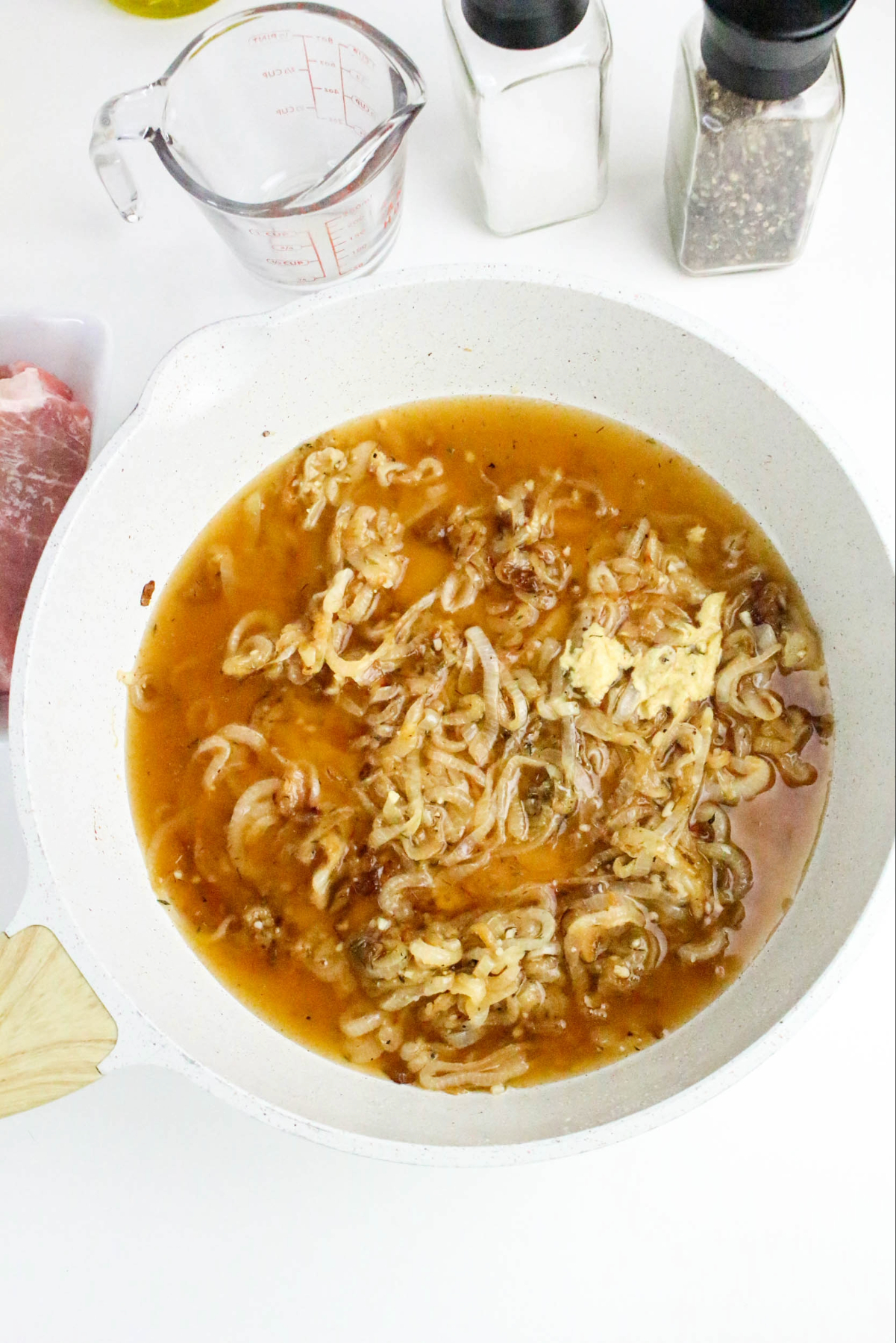 Adding beef broth to caramelized onions in a white skillet.