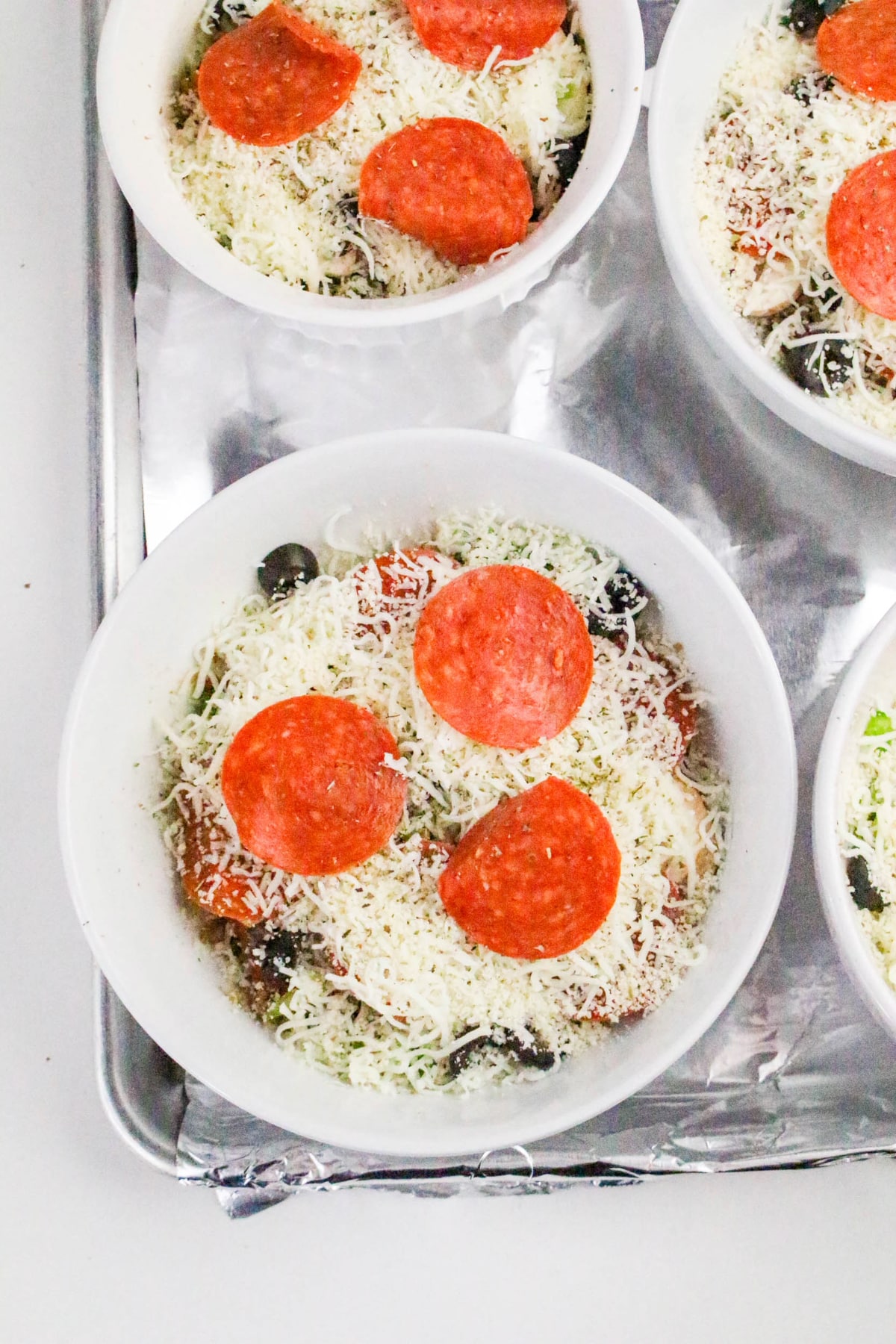 Ramekins filled with pizza toppings and cheese on a baking sheet before going into the oven.