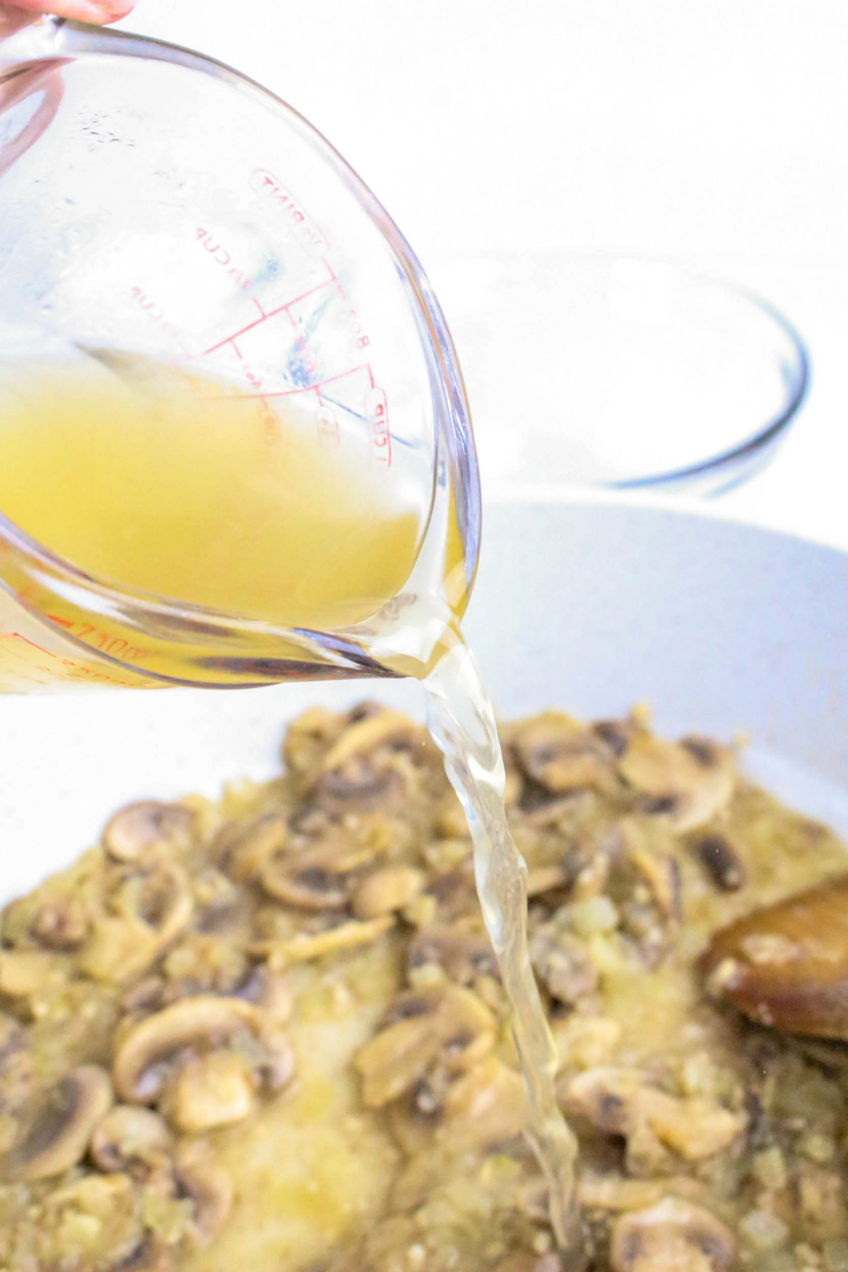 A glass measuring cup with broth poured into a mushroom sauce.