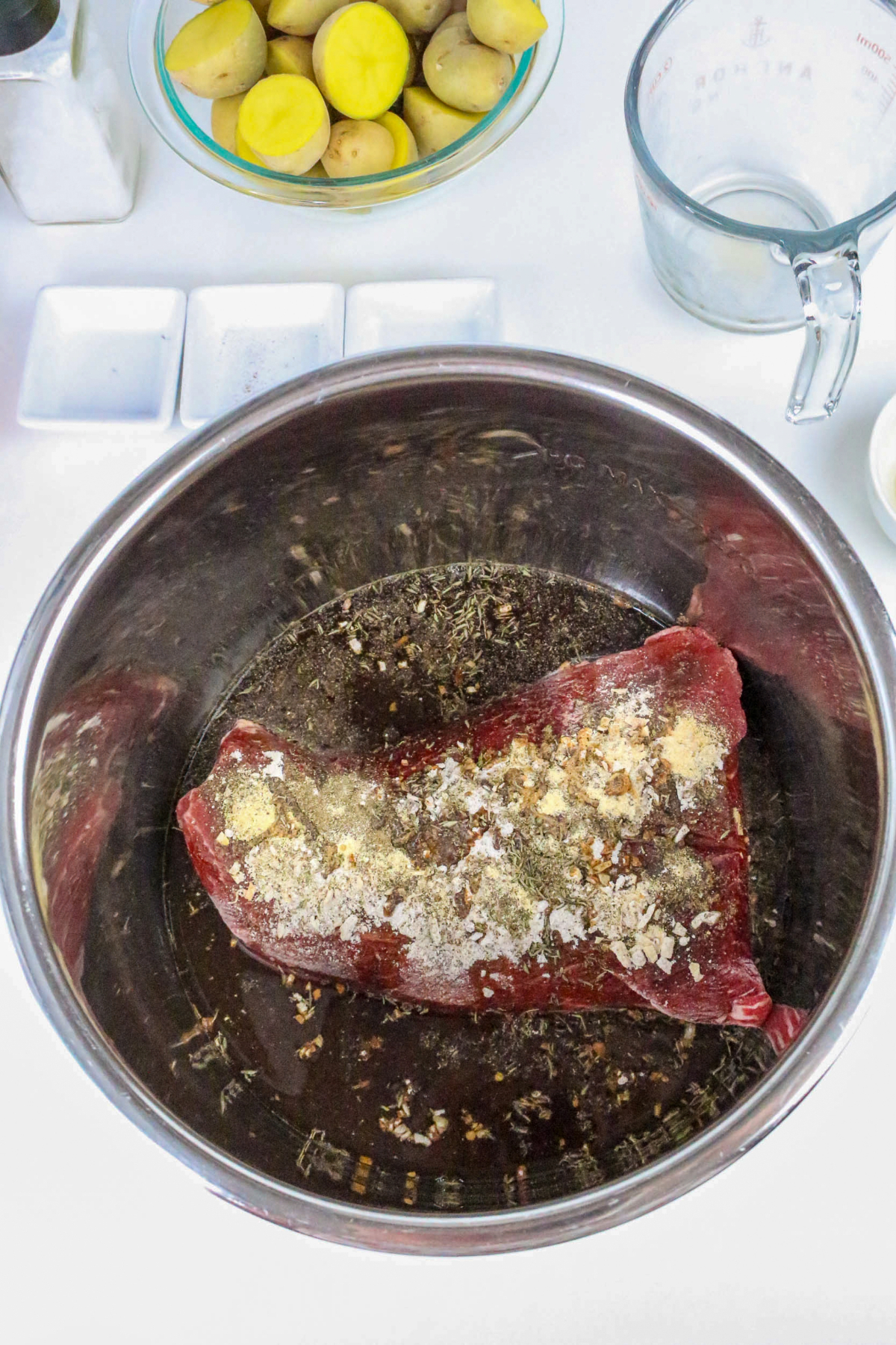 Stainless steel insert of an instant pot with frozen beef and spices.