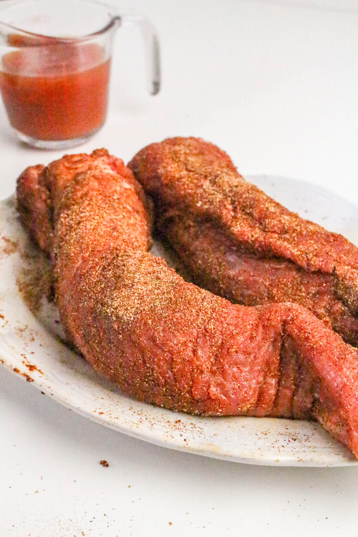 Pork tenderloin topped with spices on a white platter.