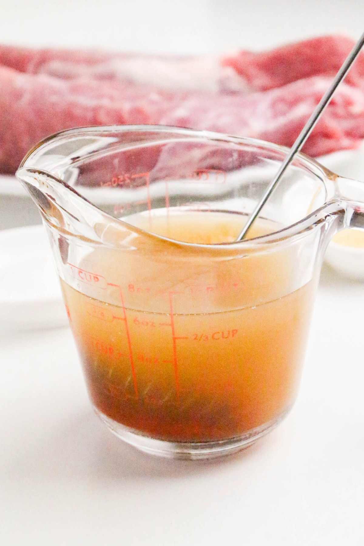 Spices mixed with chicken broth in a glass measuring cup.