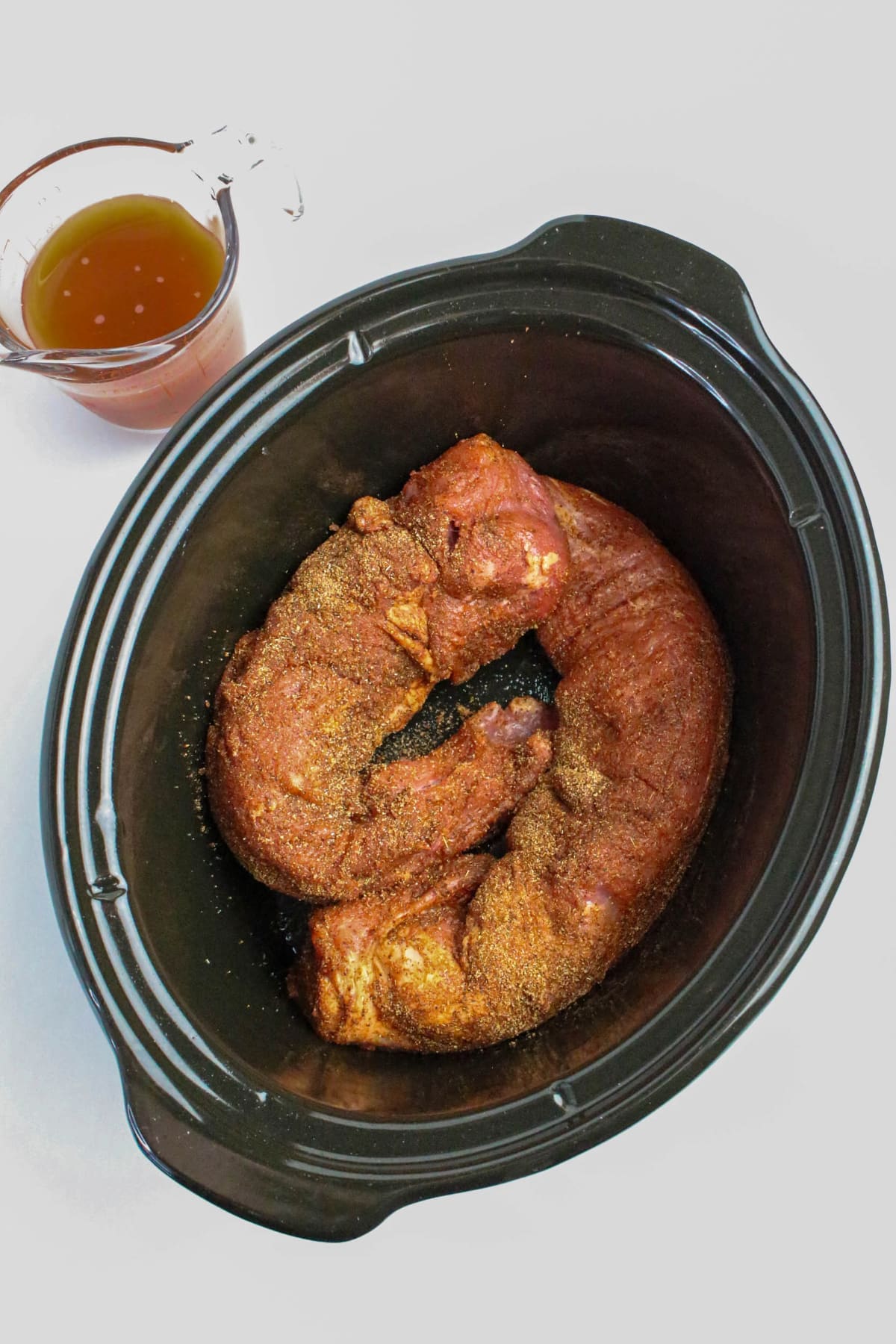 Pork tenderloin in a slow cooker with spices before cooking.