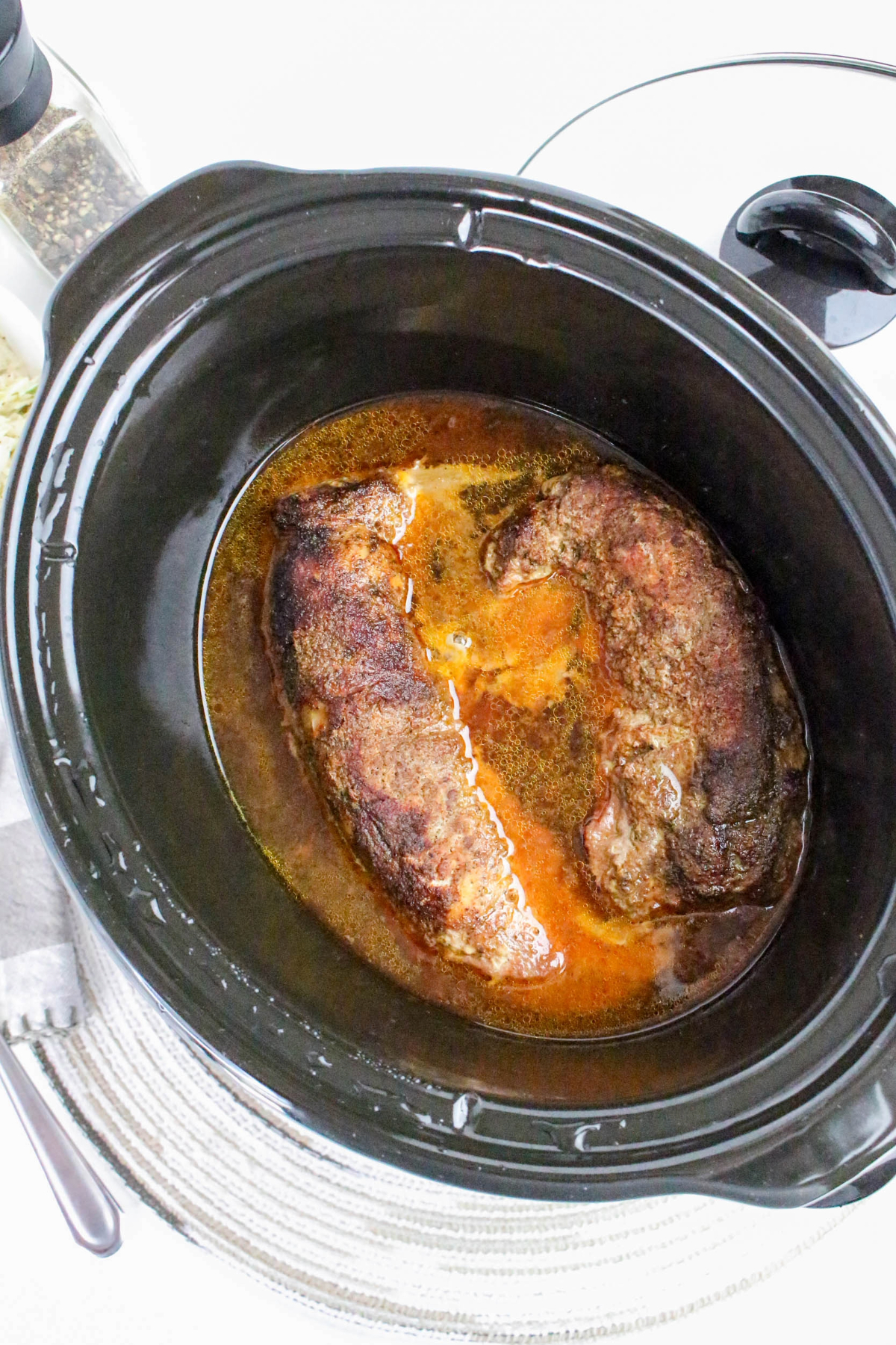 Pork tenderloin in a black slow cooker before shredding.