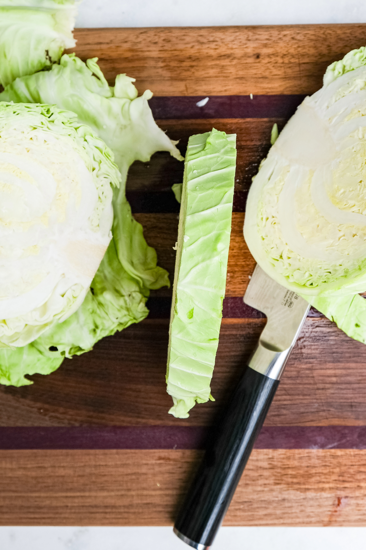 A cabbage head on a brown cutting board cut into 1-inch slice.