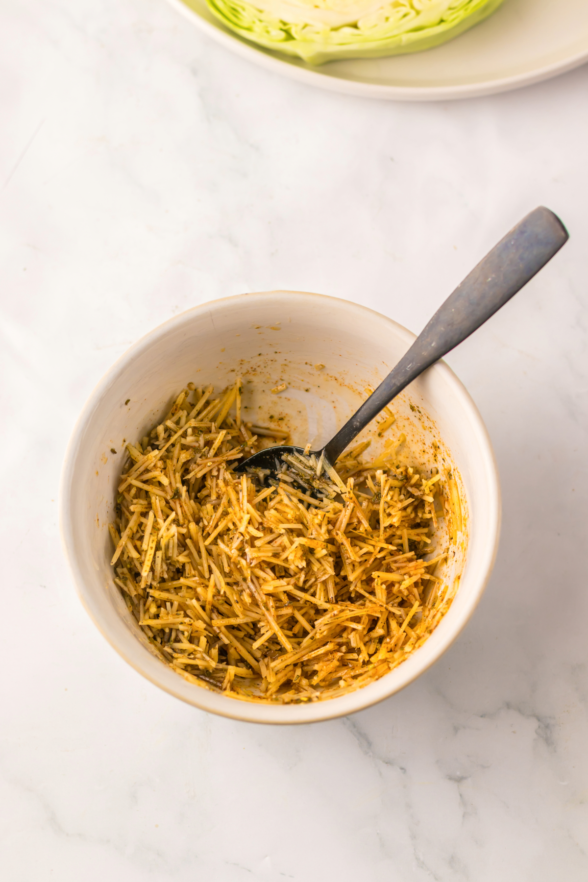 Shredded parmesan cheese in a small white mixing bowl with spices before adding it to sliced cabbage steaks.